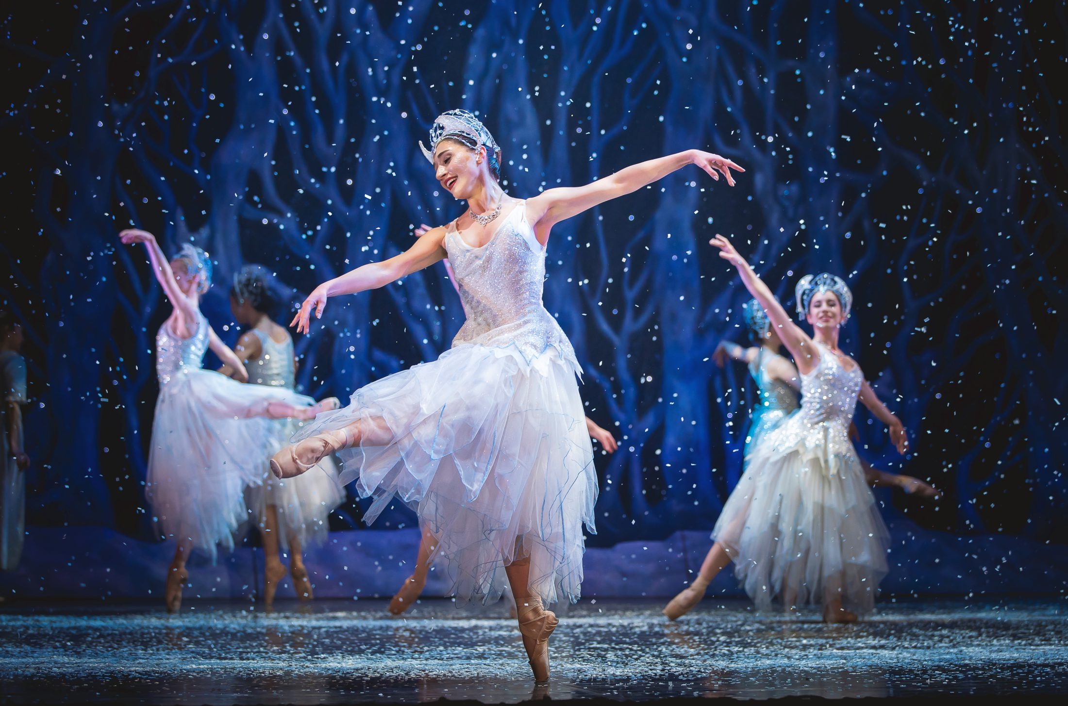 Photo of ballerinas dancing on a snowy stage, wearing white dresses.