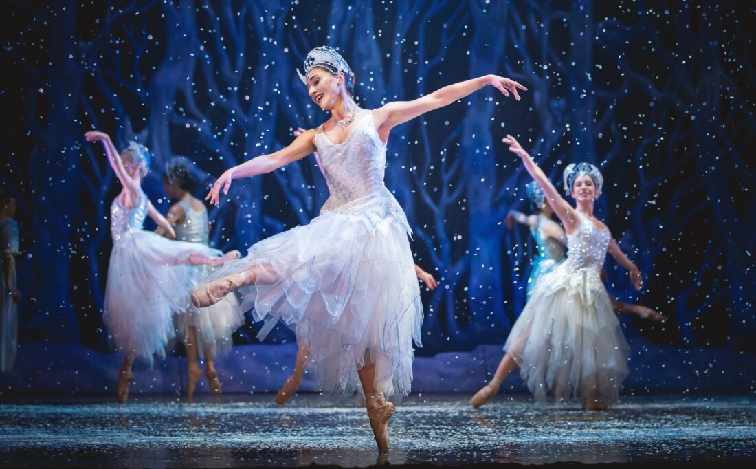 Photo of ballerinas dancing on a snowy stage, wearing white dresses.