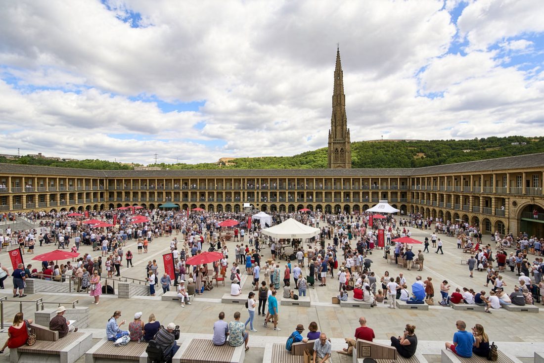Photo of The Piece Hall’s huge courtyard, bustling with people under scattered white and red umbrellas.