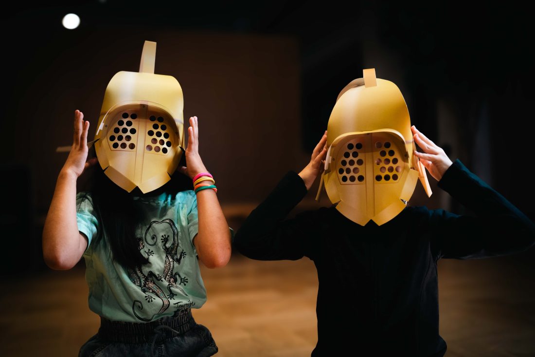 Photo of two people wearing large, cardboard gladiator helmets.