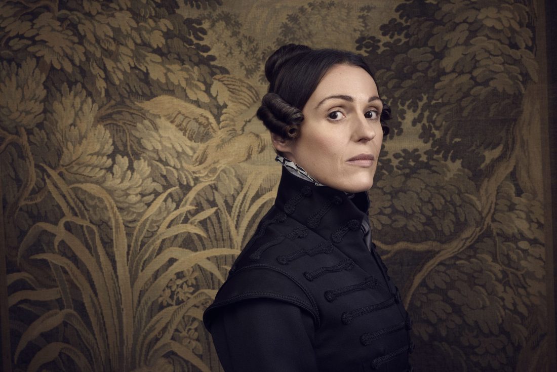 Photo of the character of Anne Lister from the period drama ‘Gentleman Jack’, dressed in black against leafy wallpaper.