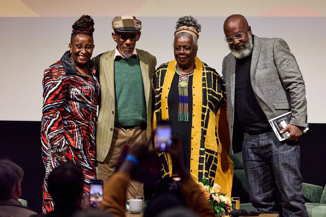 Photo of four people smiling and posing together for photographs. The two women are wearing colourful clothes and the two men are in smart jackets.