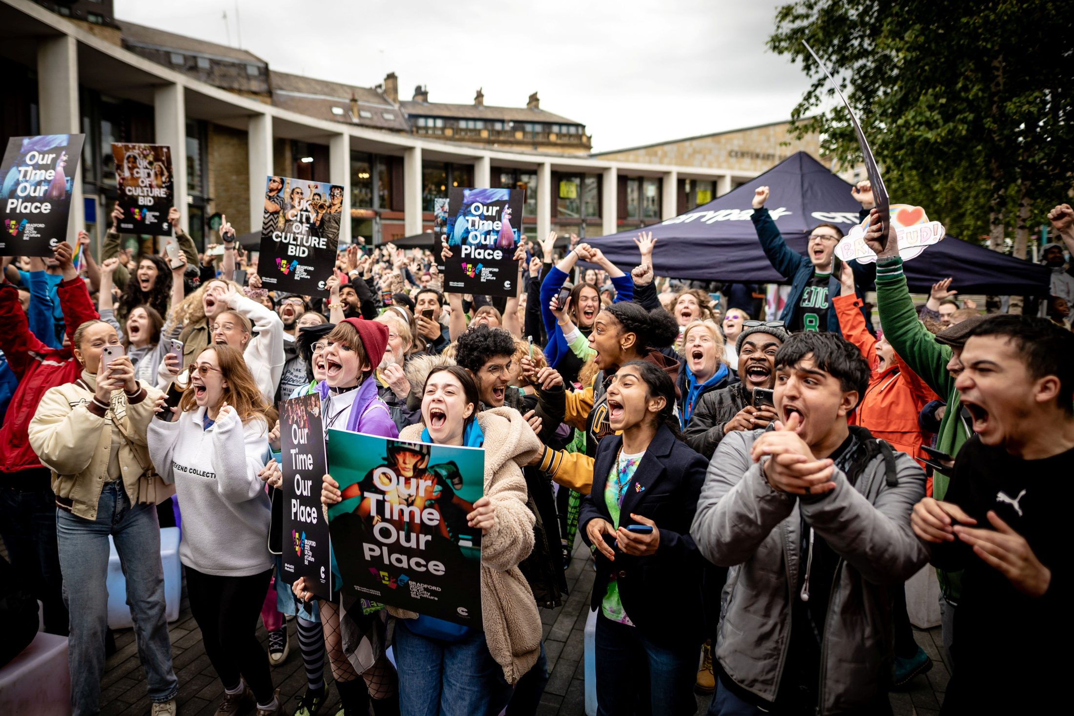 Photo of a crowd of young people gathered outside, cheering exultantly. Many hold signs reading, ‘Our time our place’.