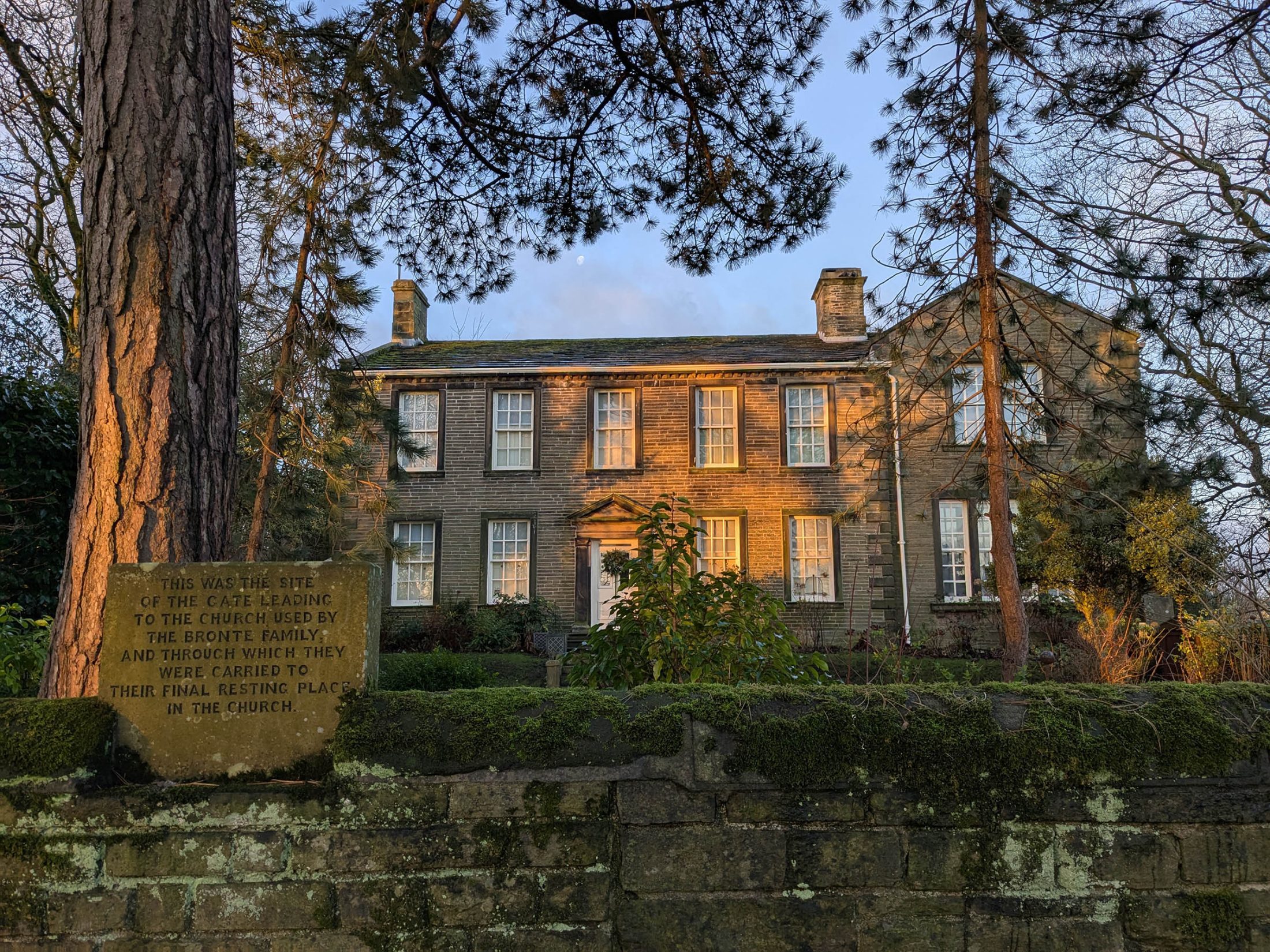 Photo of the Brontë Parsonage Museum – an 18th-century house surrounded by trees – in the golden morning light.