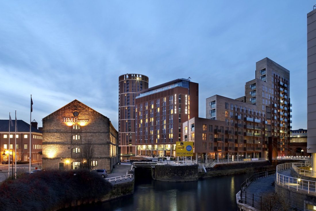 Twilight photo of Granary Wharf – a dock with old warehouses and modern buildings lining it, their lights reflecting in the water.