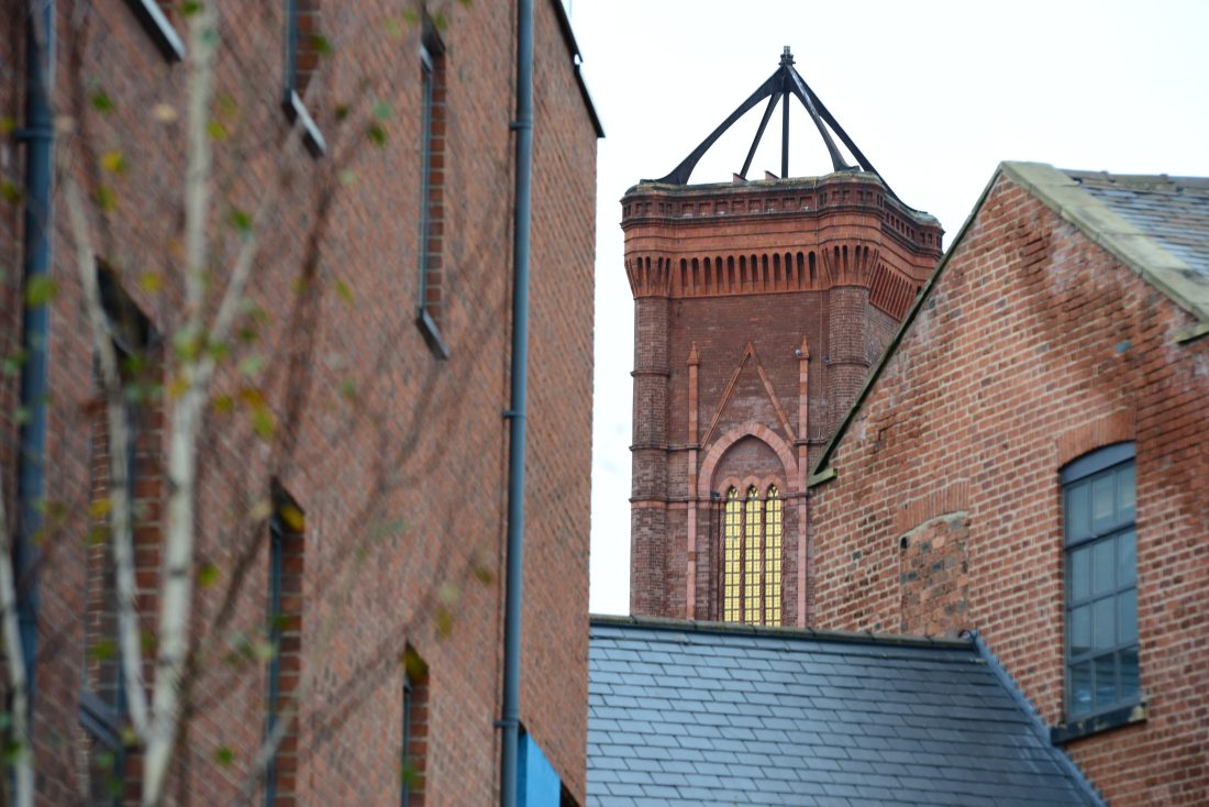 Photo of a red-brick tower with gleaming windows in Holbeck Urban Village, with red-brick warehouses in the foreground.