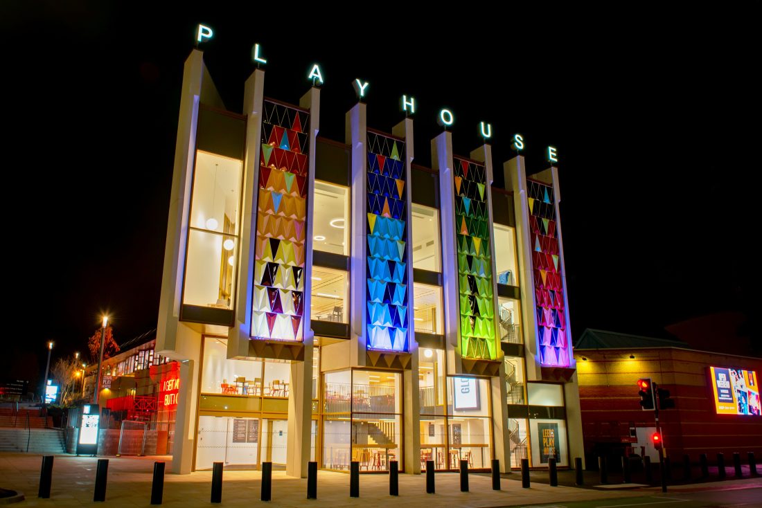 Photo of the colourful front of Leeds Playhouse at night, lit up from the inside.