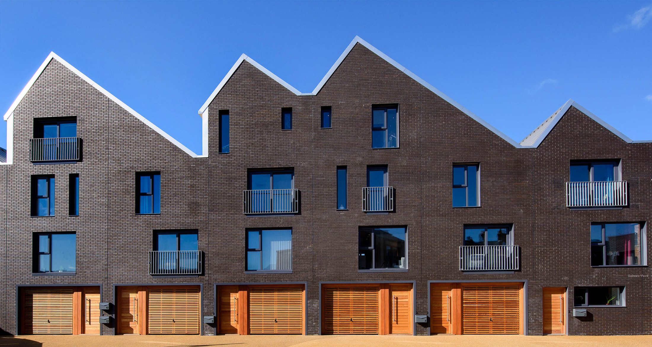 Photo of Little Kelham in Sheffield on a sunny day – an attractive, modern residential block with black walls, sloping roofs, big windows and bright wooden doors.