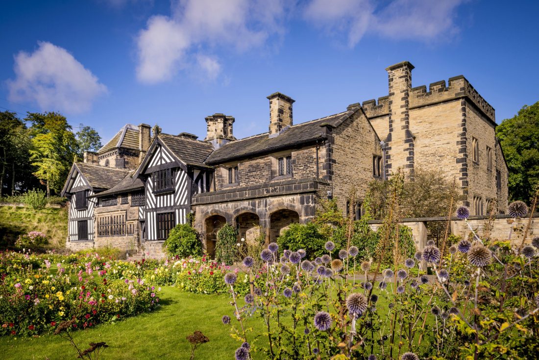 Photo of Shibden Hall, an old stone building with black-and-white timber cladding, on a sunny day surrounded by pretty gardens.