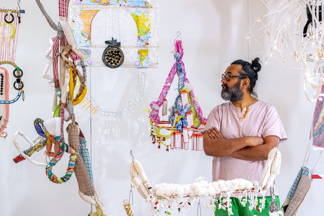 Photo of a man with a beard and glasses looking at the interesting textiles sculptures hanging all around him.