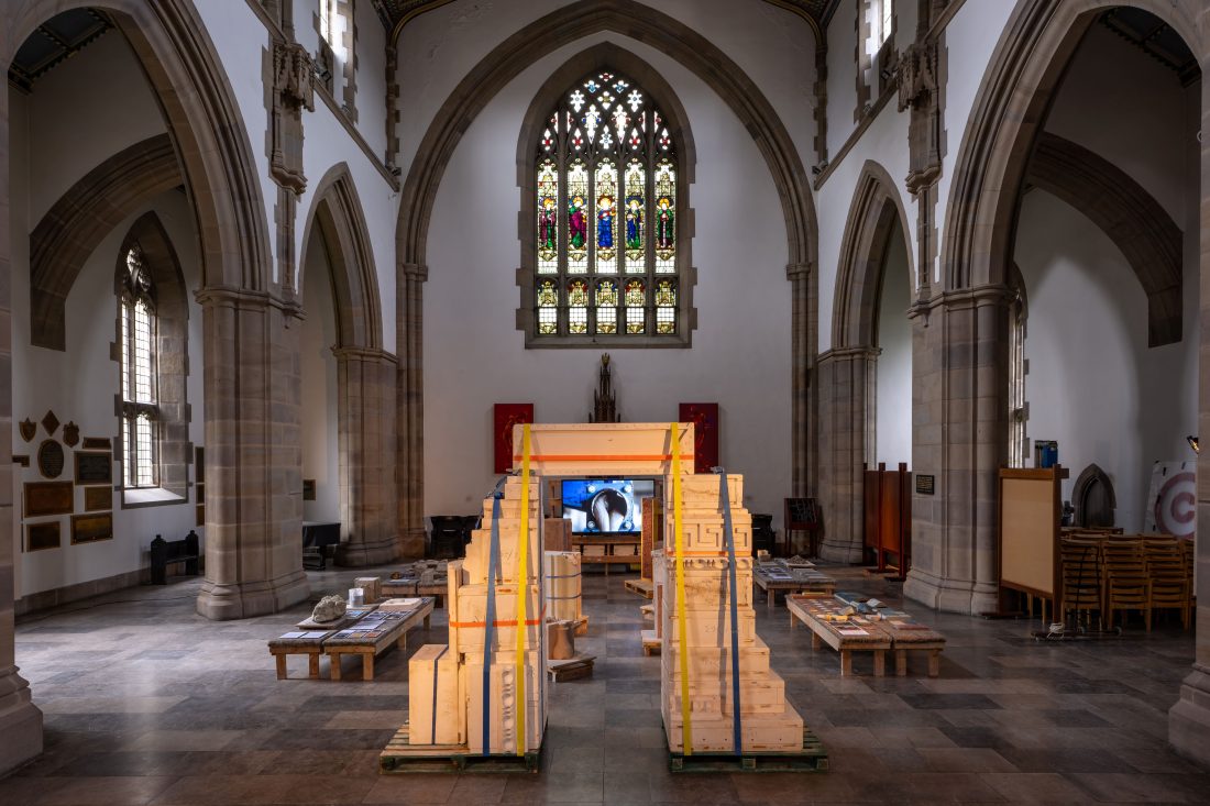 Photo of an archway made from wooden boxes in a church, with a TV visible through it.