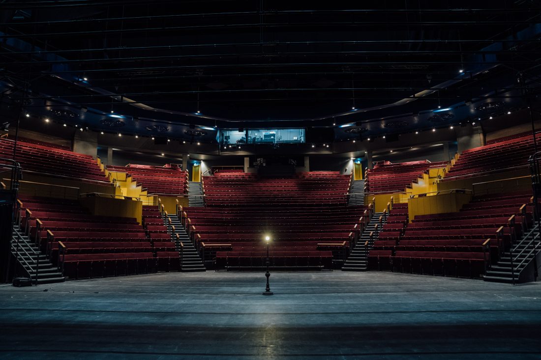 Photo of an empty stage at Leeds Playhouse looking out to empty seats, with a single lit lightbulb on a tall stand in the middle.