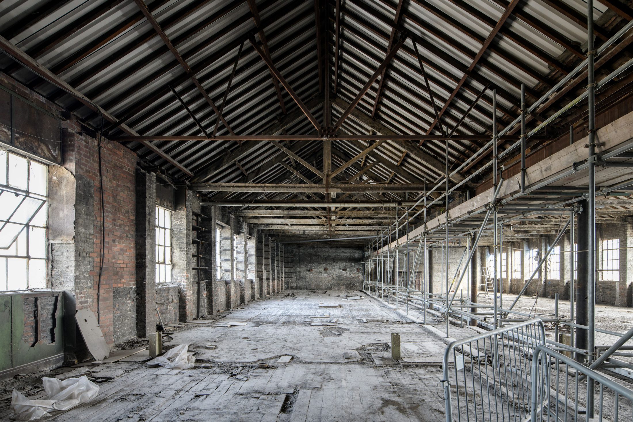 Photo pointing down the inside of the Pattern Shop before work was completed – a long, old factory with crumbling floors and metal beams.