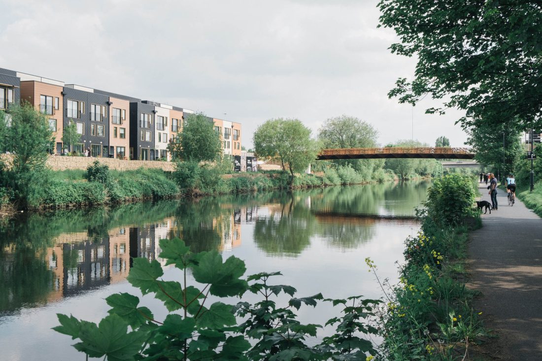 Photo of a lush canal, overlooked by a row of modern, attractive, black and orange apartments.