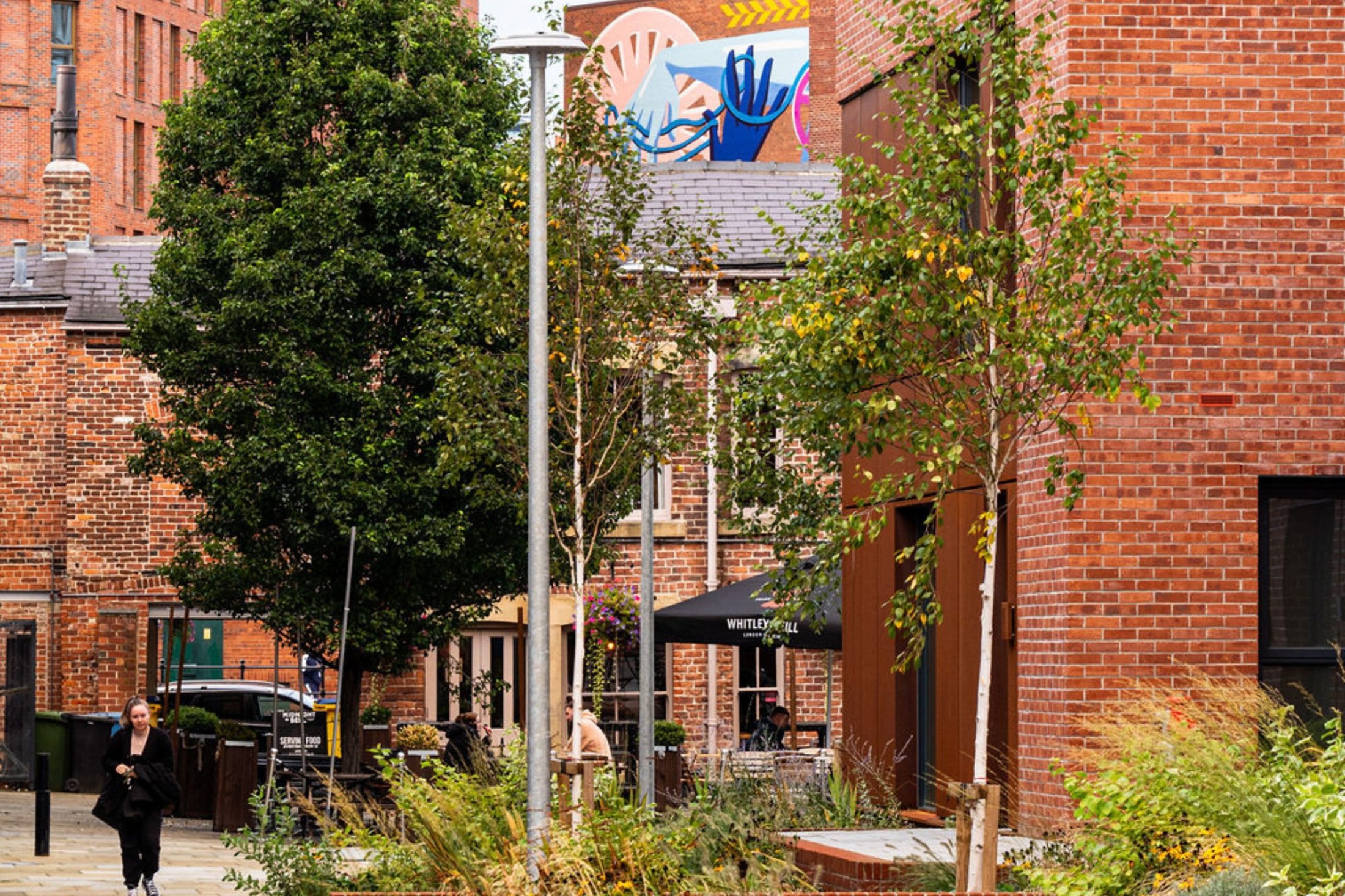 Photo of modern, red-brick apartments, with trees and green plants in the foreground.