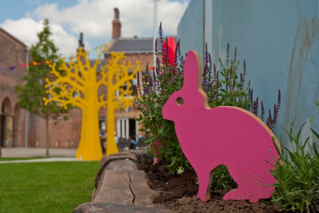 Photo of a pink, wooden bunny in Wonderwood at Holbeck Urban Village, with grass, plants and trees in the background.